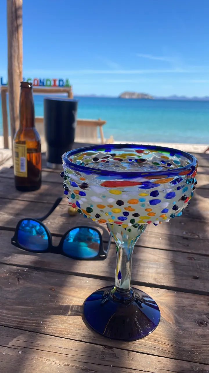 Large margarita in a blue-rimmed glass on a wooden deck overlooking the bay