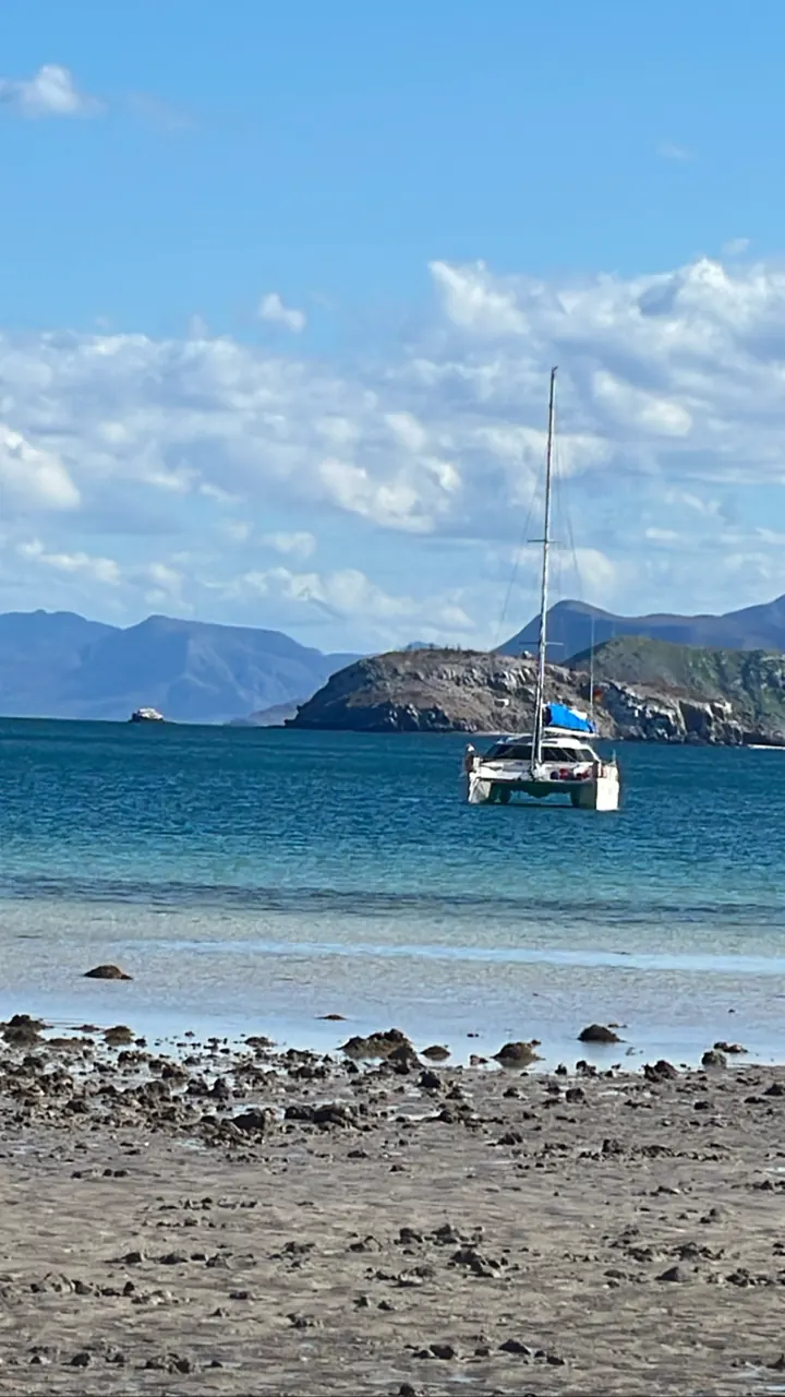 Sailboat anchored off a pebbly beach with islands behind