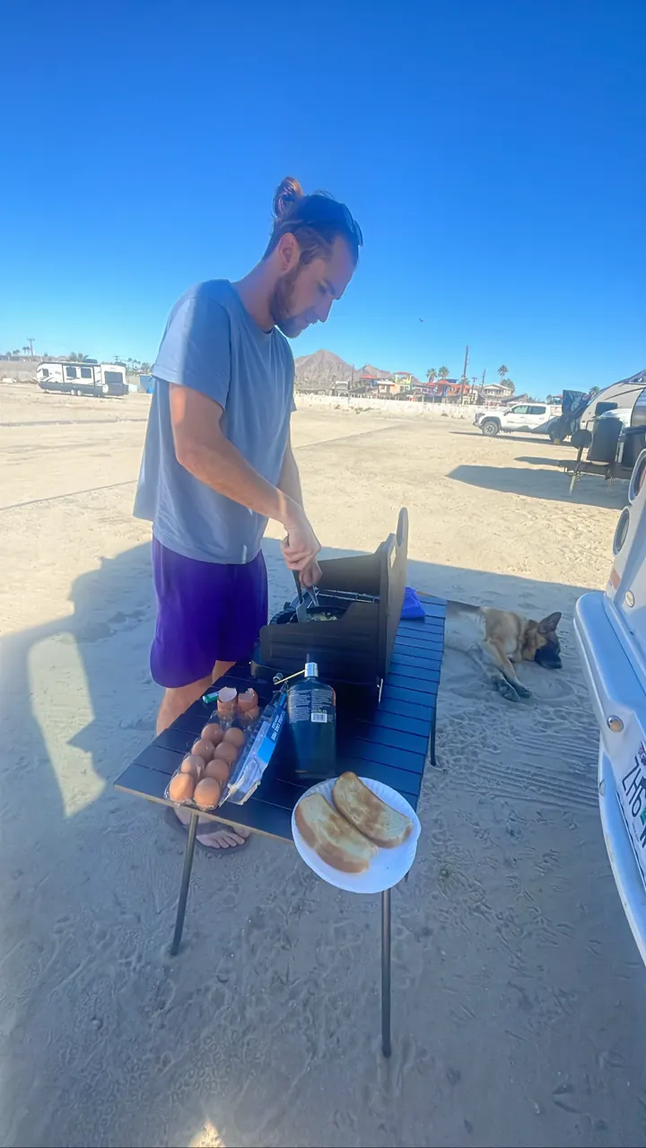 Colin cooking on a camp stove set up beside the van on the beach
