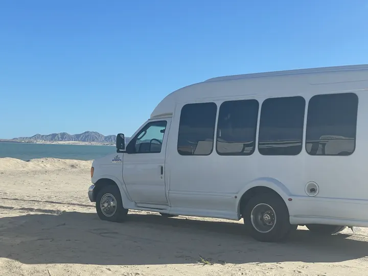 Our white camper van parked on a sandy beach with water and hills behind
