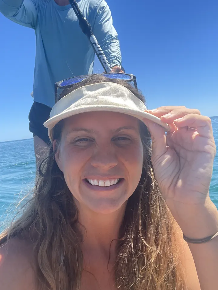 Angela smiling in a white visor and sunglasses on a boat