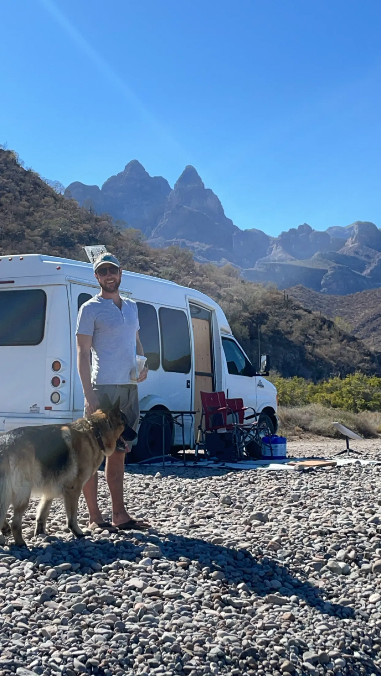 Colin and Jack, our German Shepherd, beside our camper van on a gravel beach below jagged mountains