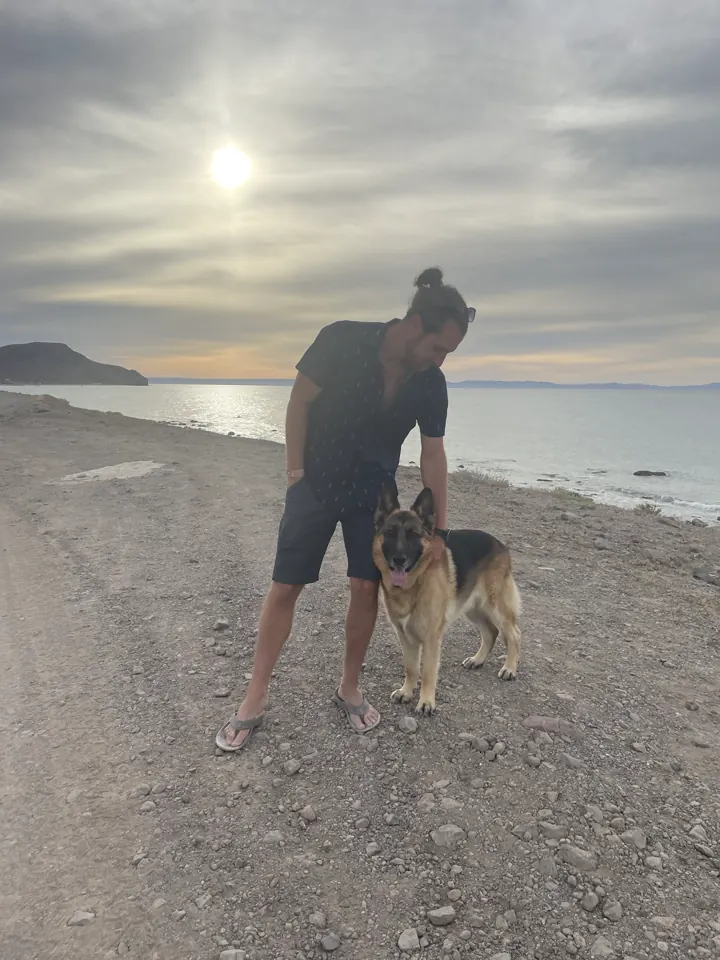 Colin standing on the beach with Jack, our German Shepherd, at his side