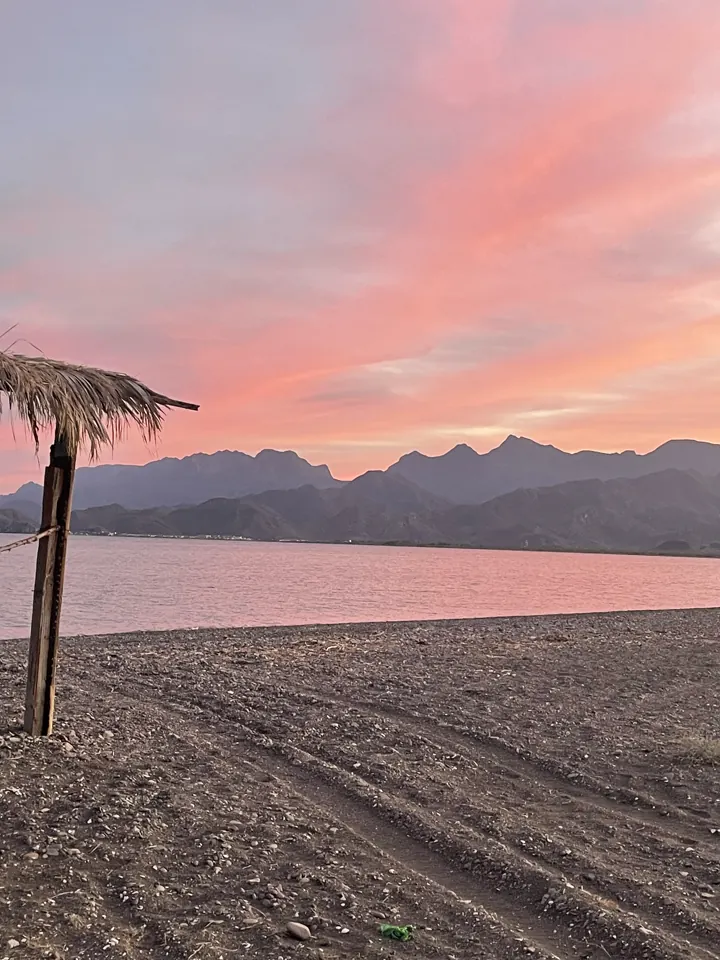 Pink and orange sunset over calm water with a thatched palapa on the beach
