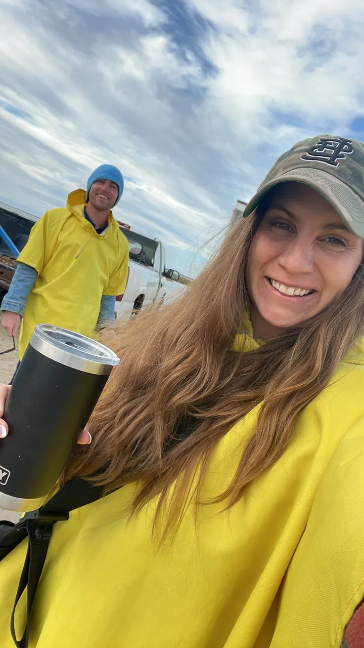 Angela in a yellow rain poncho and cap smiling on a small boat