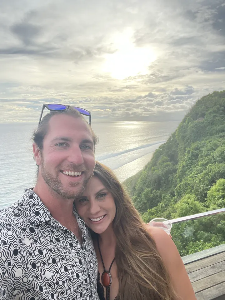 Colin and Angela taking a selfie at a cliff-top viewpoint with green hills and sea