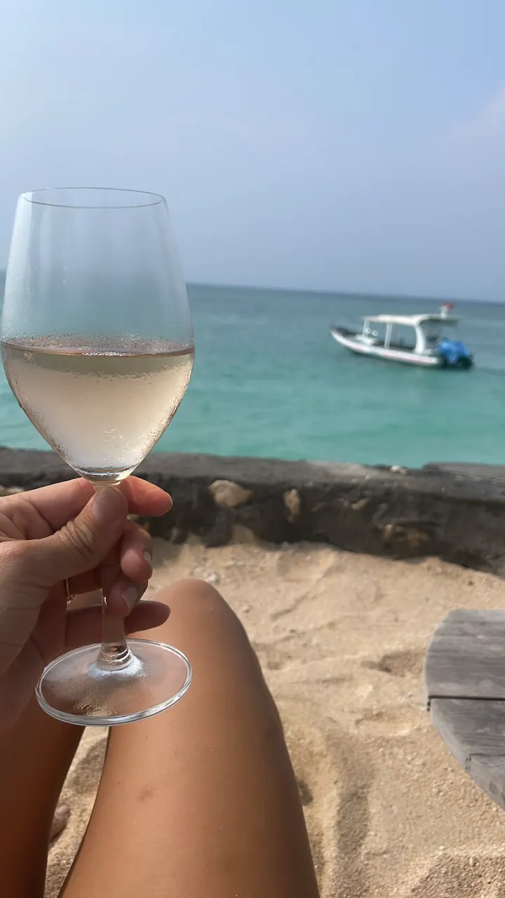 Glass of white wine held up over a turquoise sea with a boat in the distance