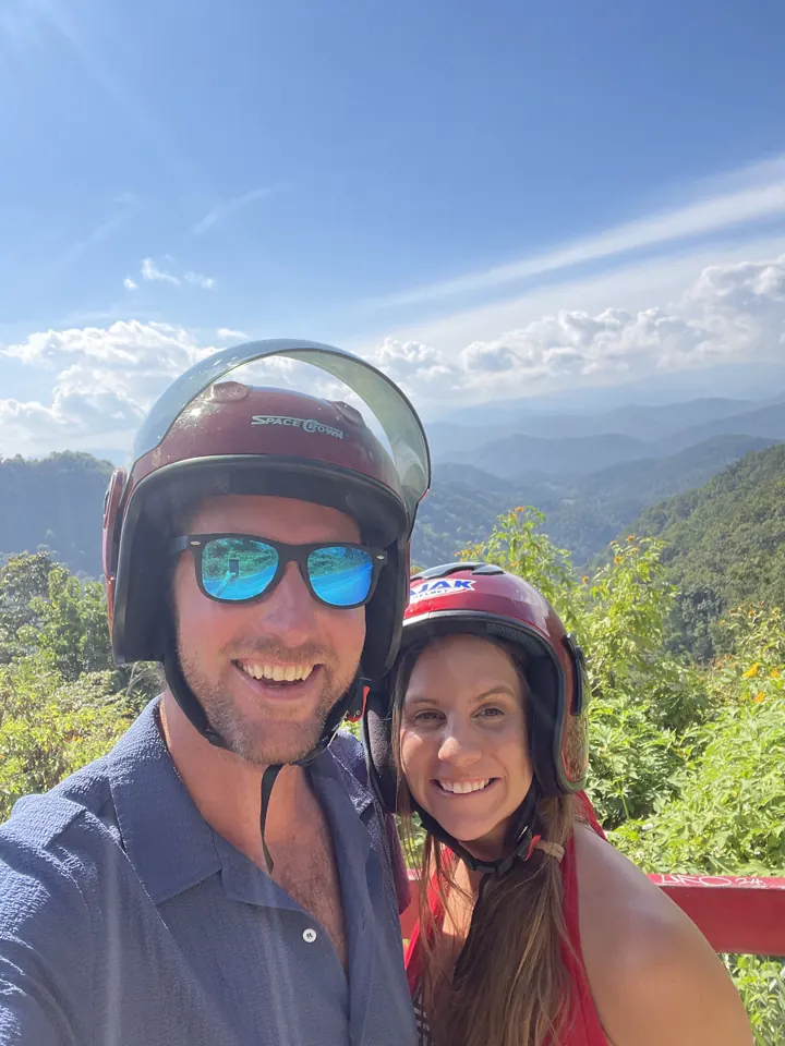 Colin and Angela in helmets and sunglasses taking a selfie with mountains behind