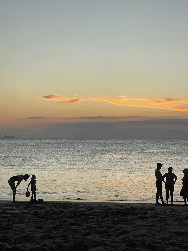 People silhouetted on the beach at dusk under a pastel sky