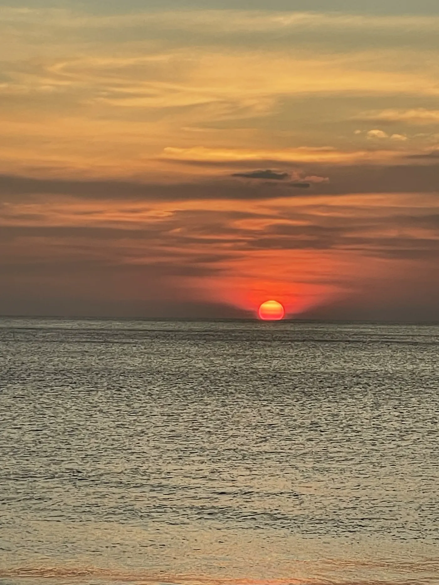 Red sun setting over calm sea under layered orange clouds