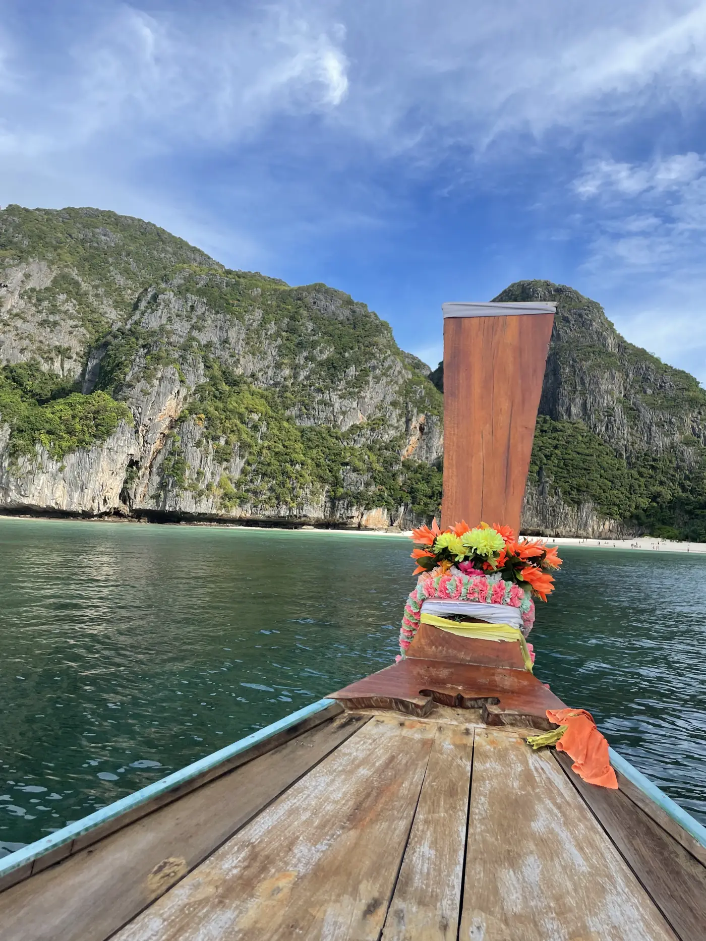 Bow of a longtail boat wrapped in colorful garlands, heading toward limestone cliffs