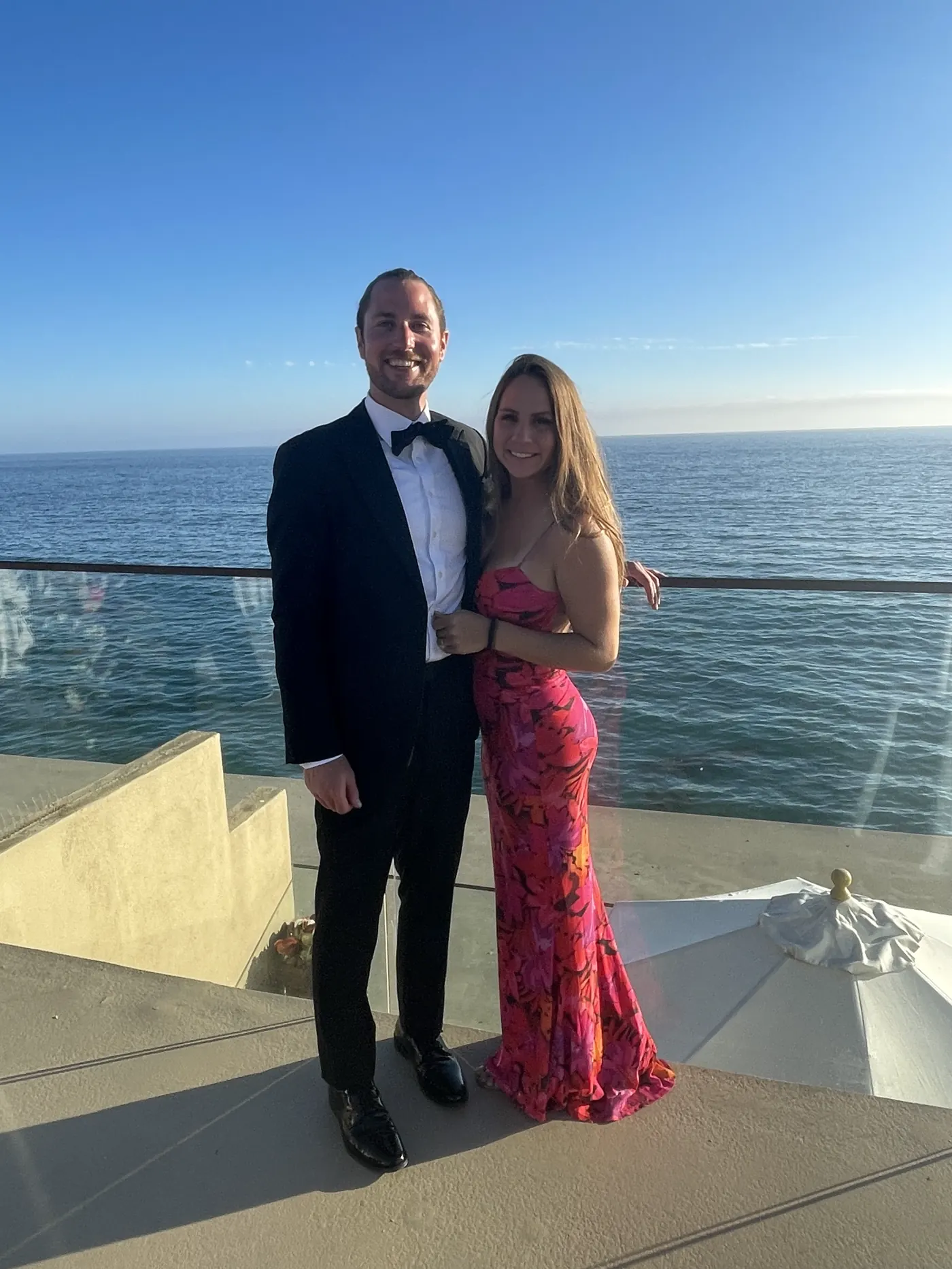 Colin in a black tux and Angela in a red sequin gown on an oceanfront terrace in Laguna Beach