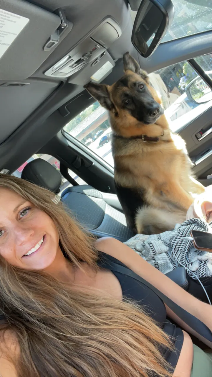 Angela smiling in the car with Jack, our German Shepherd, sitting behind her