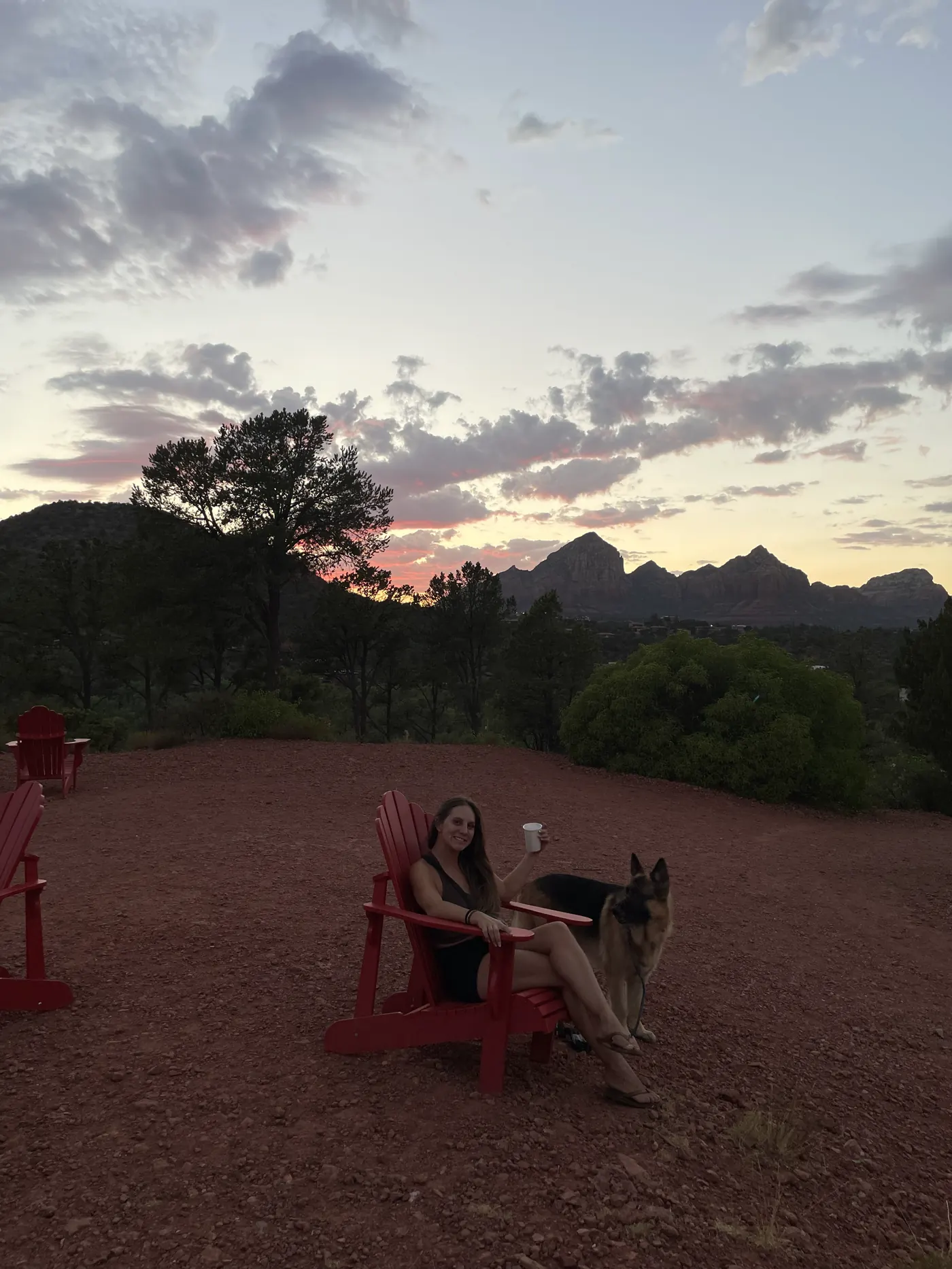Silhouettes in red Adirondack chairs with Jack, our German Shepherd, on a red dirt overlook at sunset