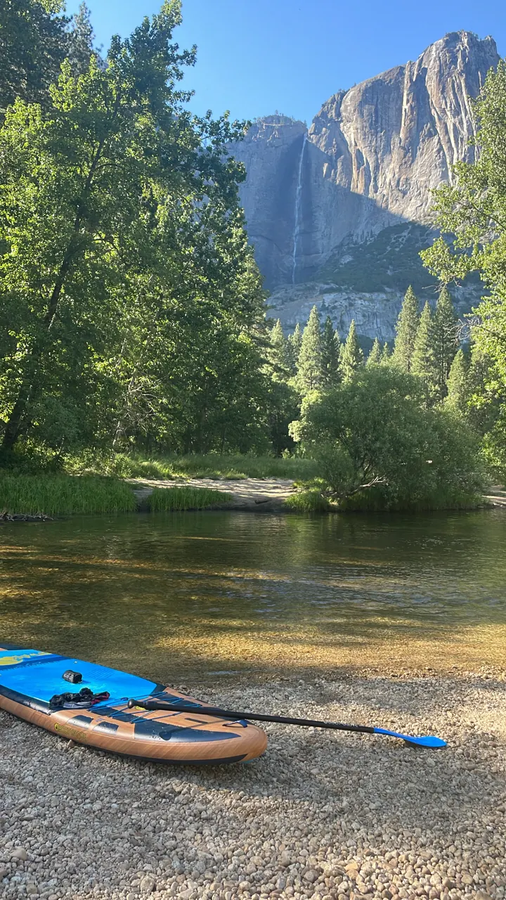 A kayak on a sandy riverbank with Yosemite Falls and granite cliffs beyond