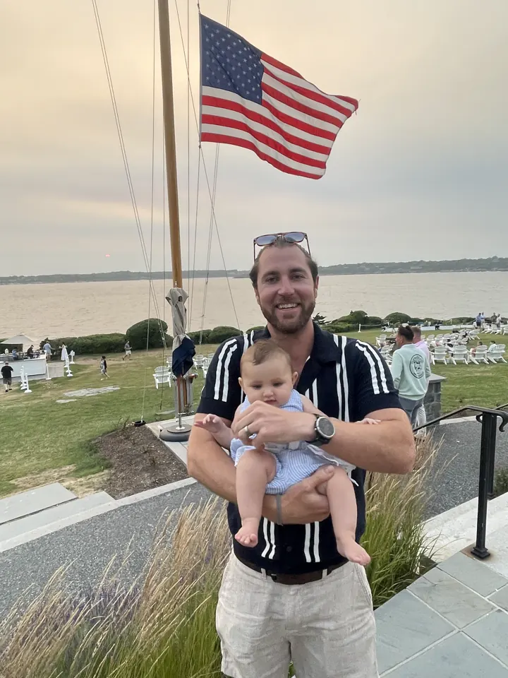 Colin holding Andi under an American flag by the bay in Newport