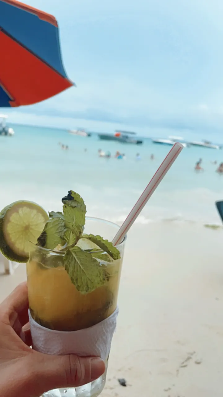 A mojito held up against a white-sand beach and blue water