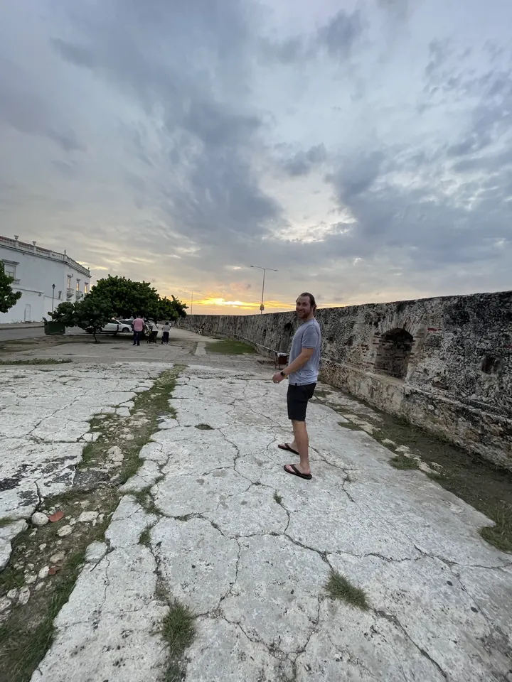 A person walking on the old city walls under a cloudy sunset sky