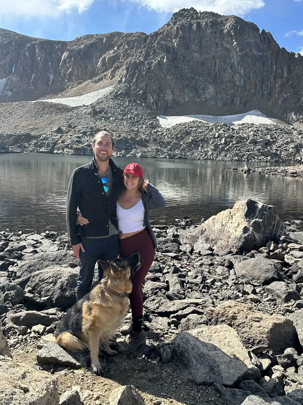 Colin and Angela with Jack, our German Shepherd, on rocks by an alpine lake below jagged peaks