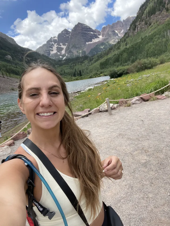 Angela smiling on a trail with the Maroon Bells behind her