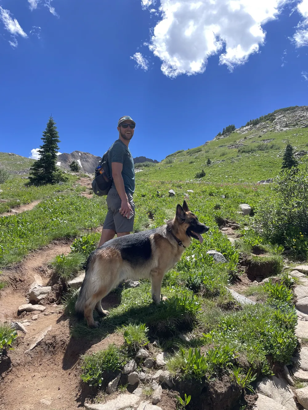 Colin and Jack, our German Shepherd, on a grassy alpine trail under blue sky