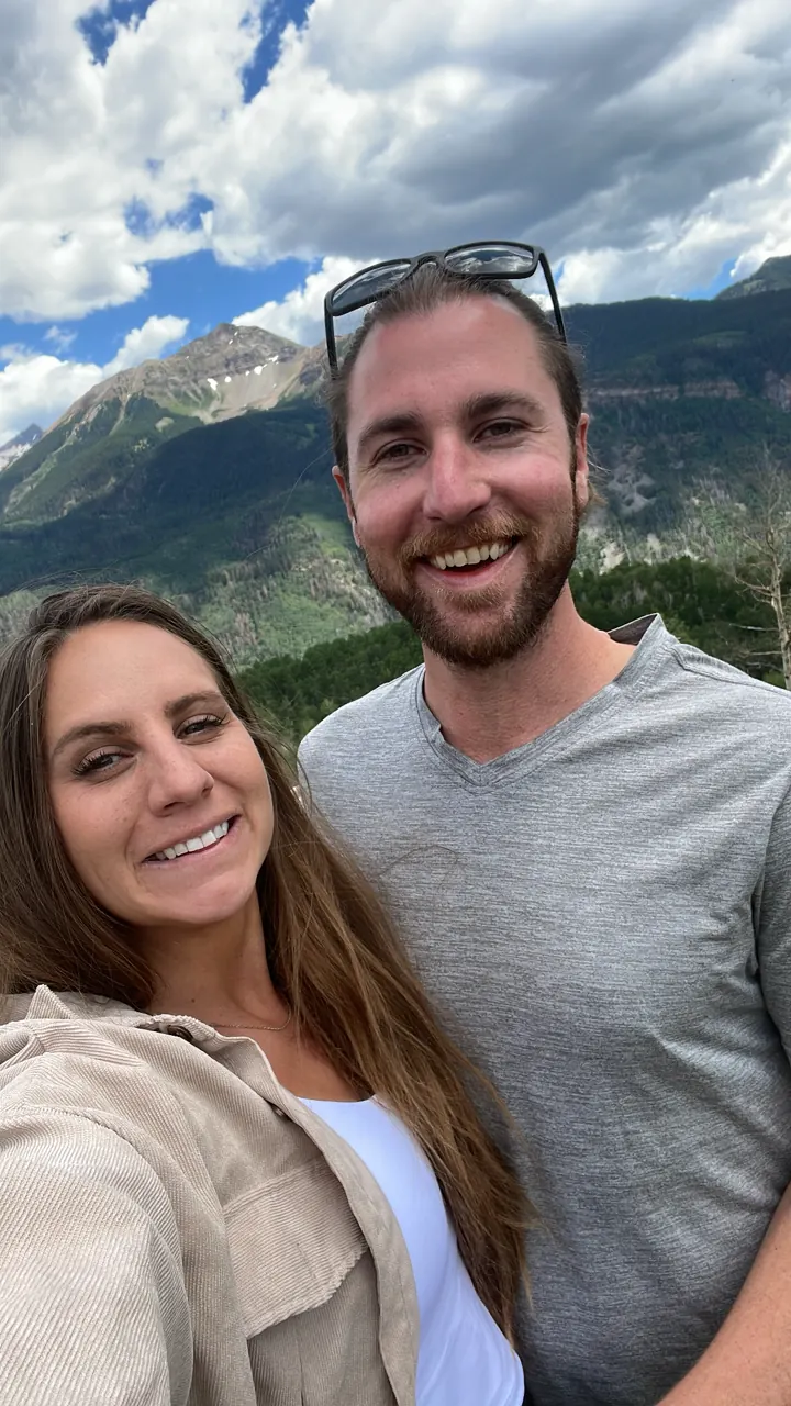 Angela and Colin smiling in a selfie with mountains behind