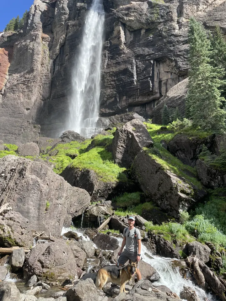Tall waterfall pouring down a cliff with a hiker on the rocks below