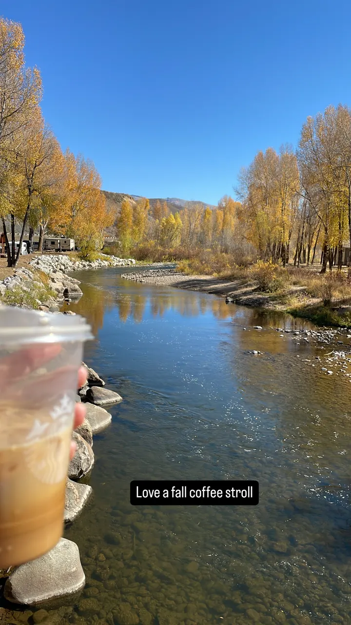 Pond reflecting golden fall trees, with a coffee cup in the foreground