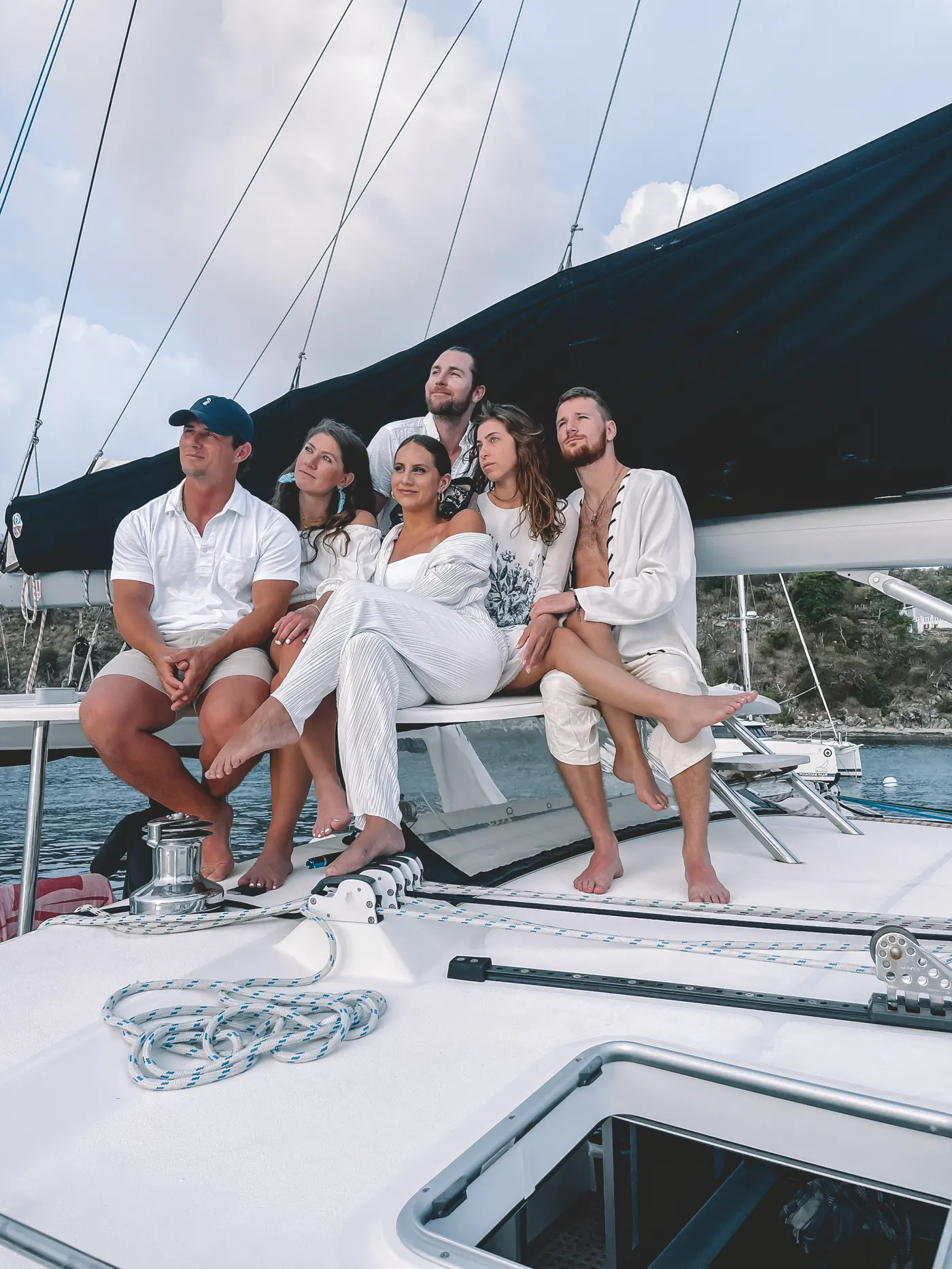 A group of friends dressed in white sitting on the bow of a catamaran