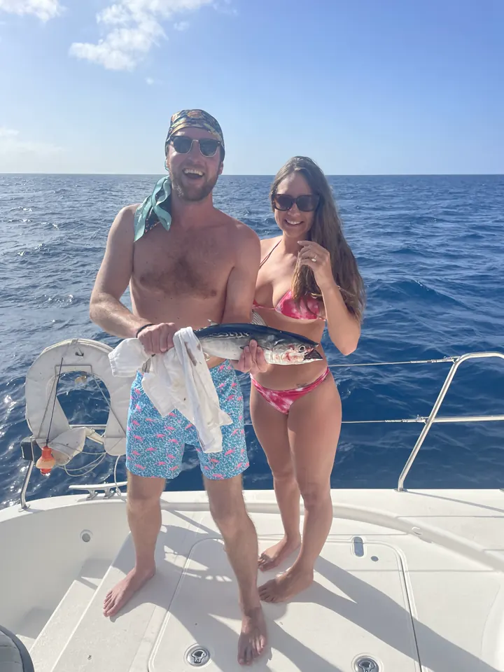 A couple on a boat deck holding up a large fish