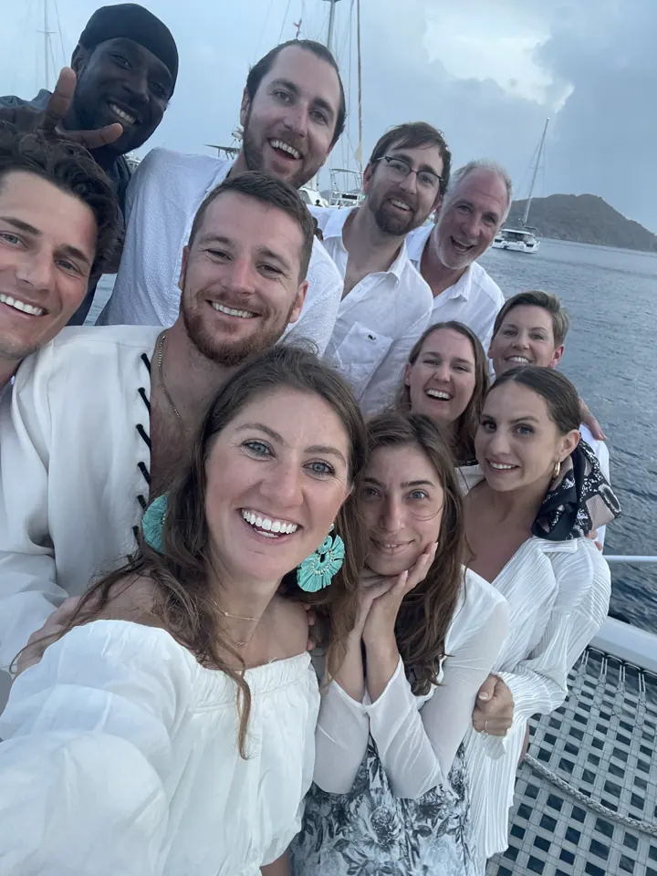 A large group of friends in white outfits taking a selfie on a boat