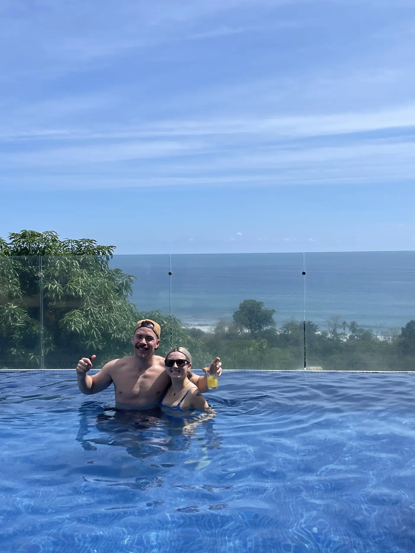 Two people in an infinity pool overlooking a green coastline and ocean