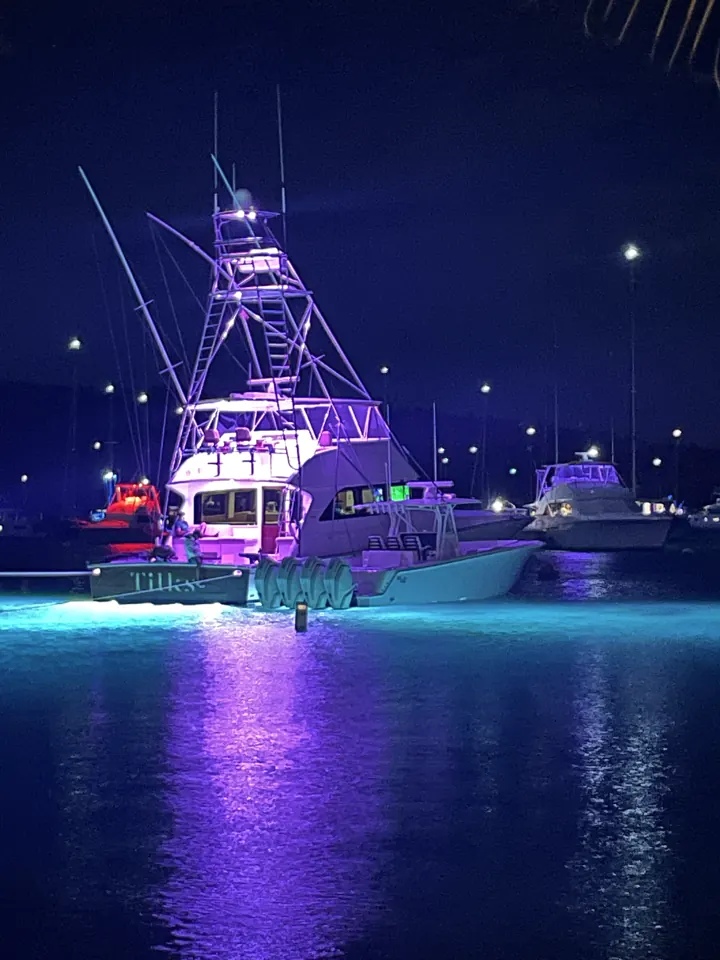 A boat glowing with purple and blue lights on dark water at night