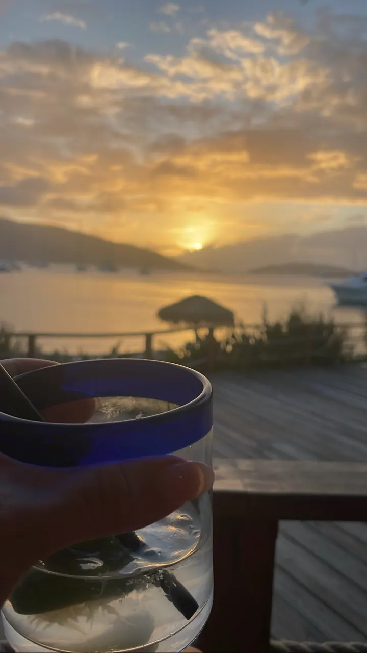 A drink glass in the foreground with a sunset over the sea