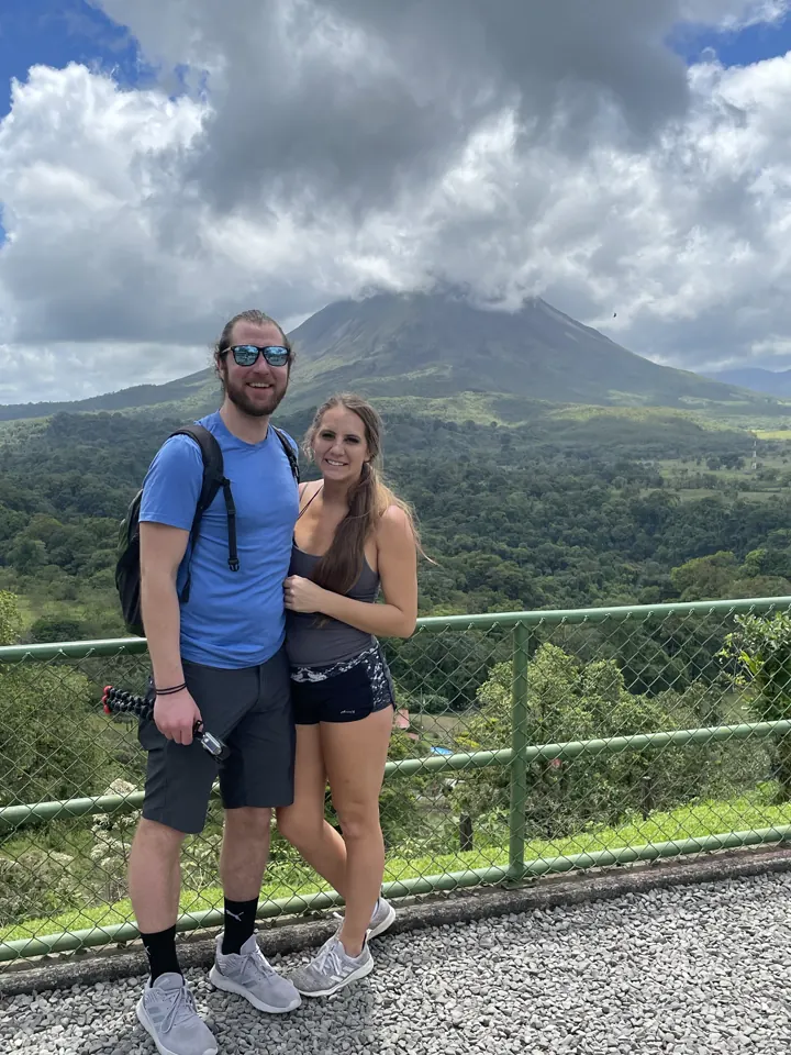 A couple standing at a lookout fence with Arenal Volcano behind them