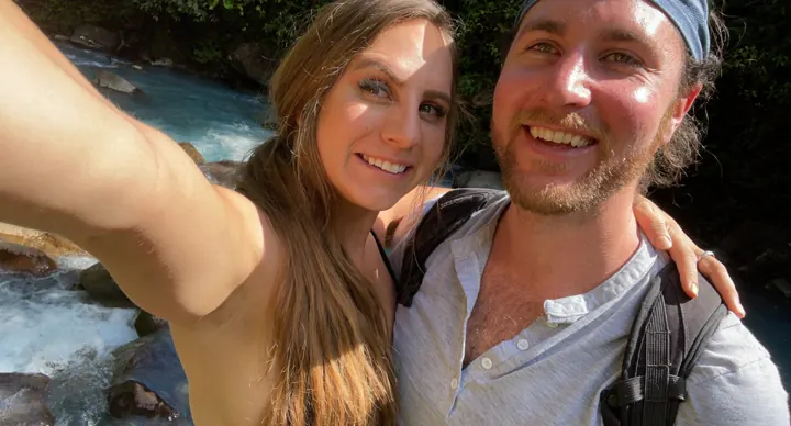 A smiling couple taking a selfie outdoors by the river