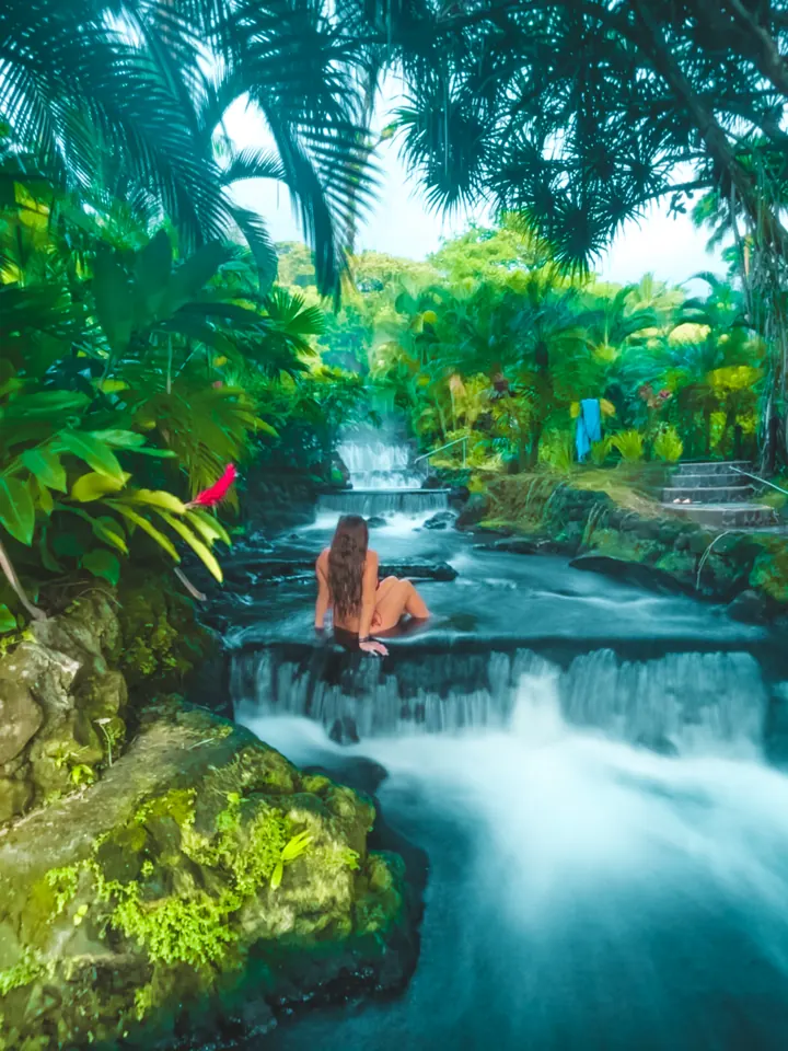 A woman sitting in a hot-spring river cascade surrounded by tropical plants