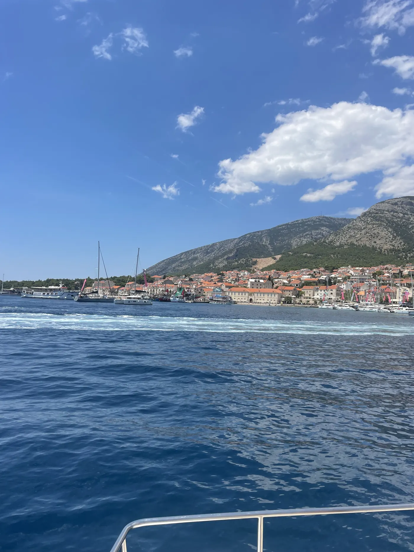 Coastal town and green hills seen across blue water from a boat