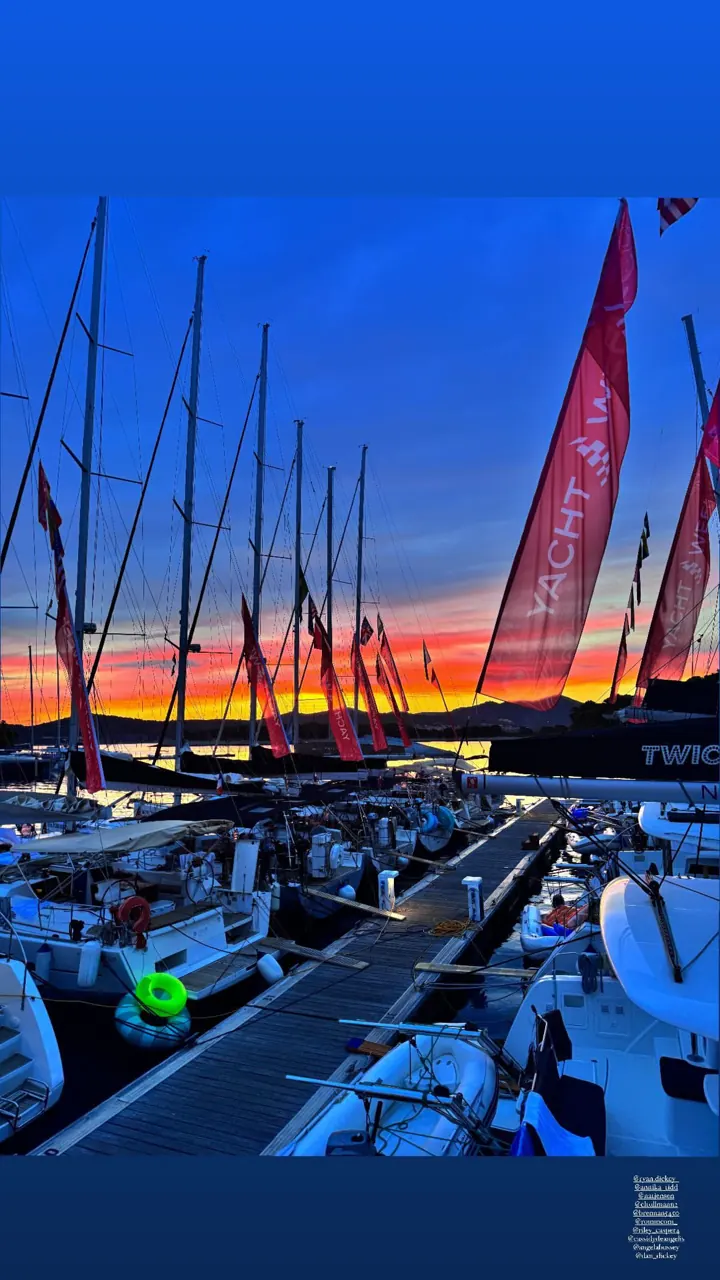 Sailboat masts silhouetted against a bright orange sunset in a marina