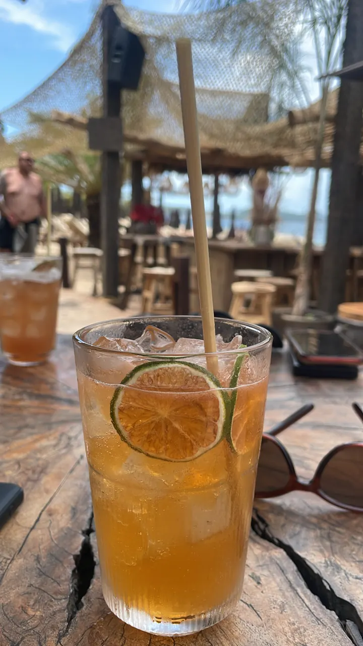 Iced amber cocktail with a lime wheel and straw on a wooden table at a beach bar