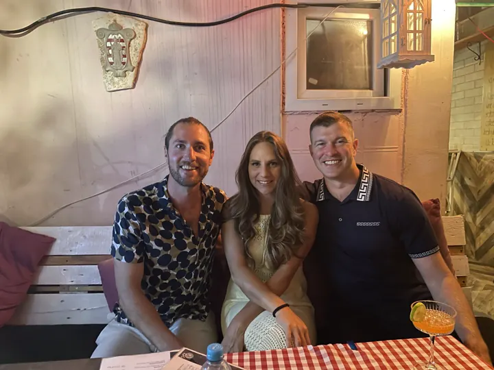 Colin, Angela and a friend smiling together at a restaurant table
