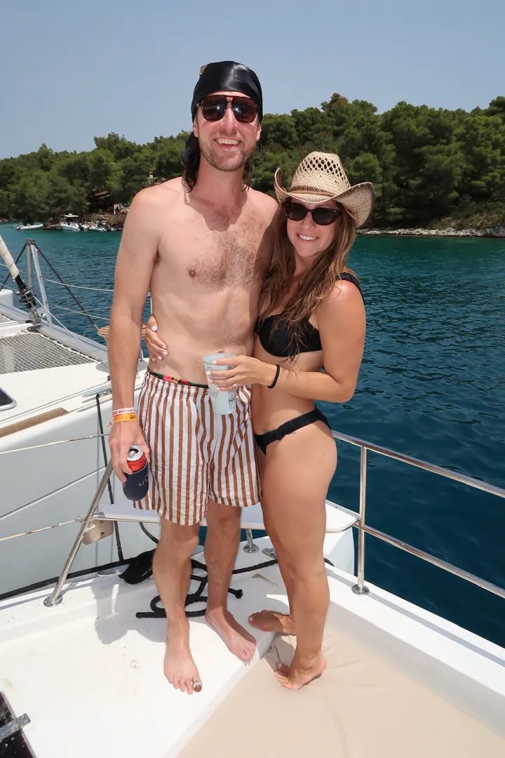 Colin and Angela, she in a cowboy hat, standing on the deck of a boat with pine-covered shore behind