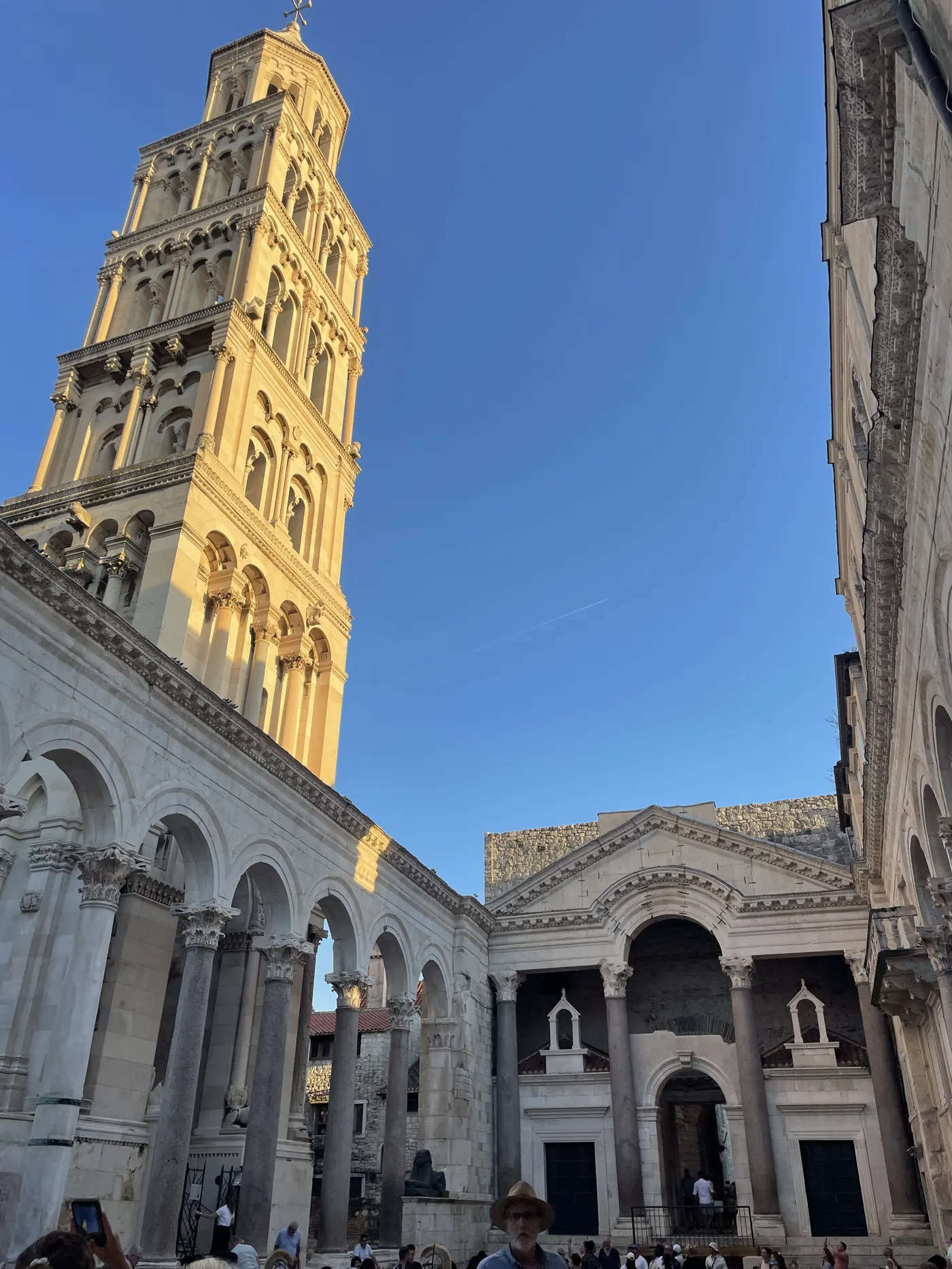 Tall stone bell tower and Roman columns of a palace square in Split, under a blue sky