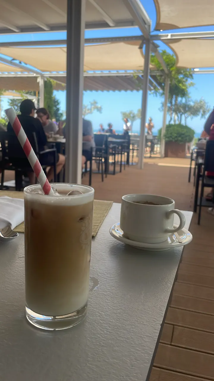 Iced coffee and a cup of coffee on a wooden table at a cafe overlooking the sea