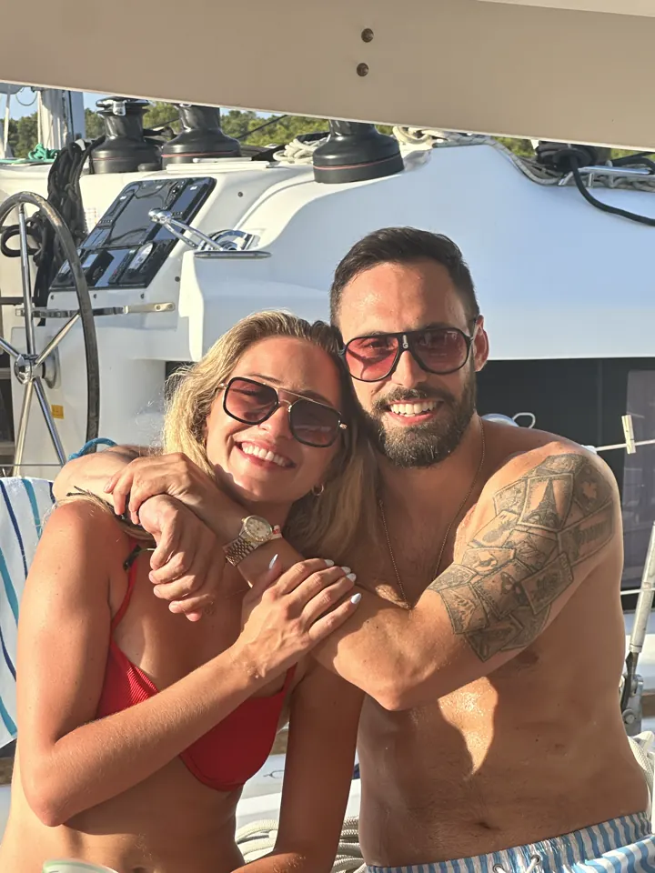 Angela hugging Colin on a boat deck, both smiling in swimwear