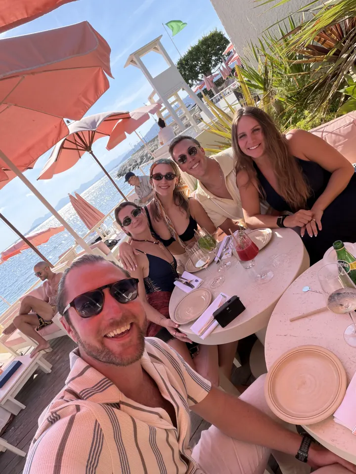 Friends taking a selfie around a lunch table under umbrellas at a beach club