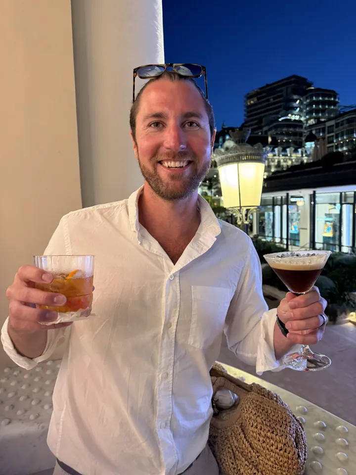 Colin in a white shirt holding a drink outdoors at night in Monaco