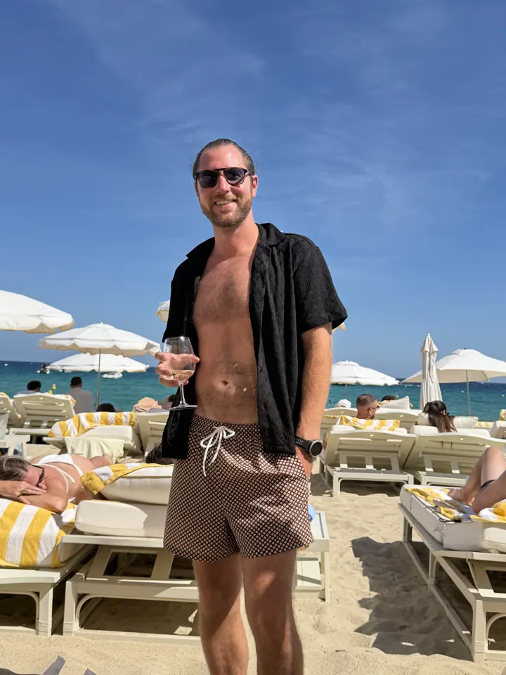 Colin in an open shirt standing among beach loungers and umbrellas
