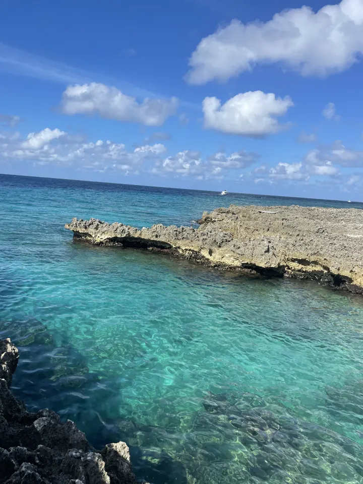 Clear turquoise water lapping against a rocky shoreline under a blue sky with clouds