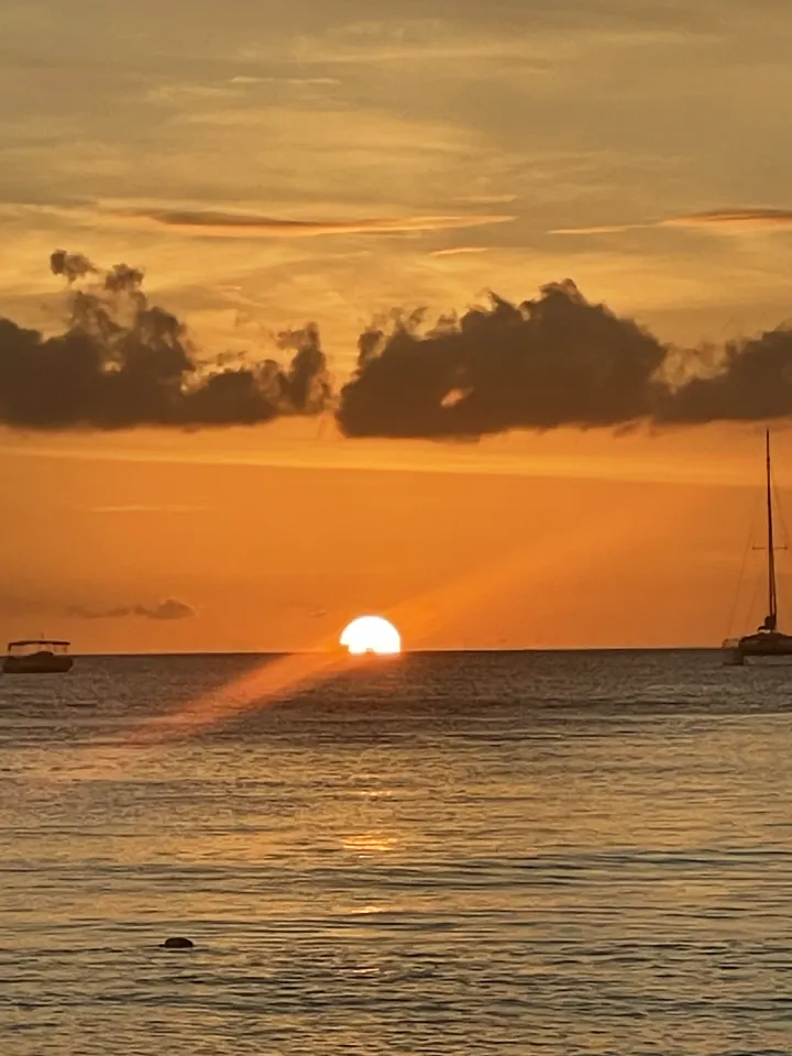 The sun sets over the sea with a sailboat silhouetted on the horizon